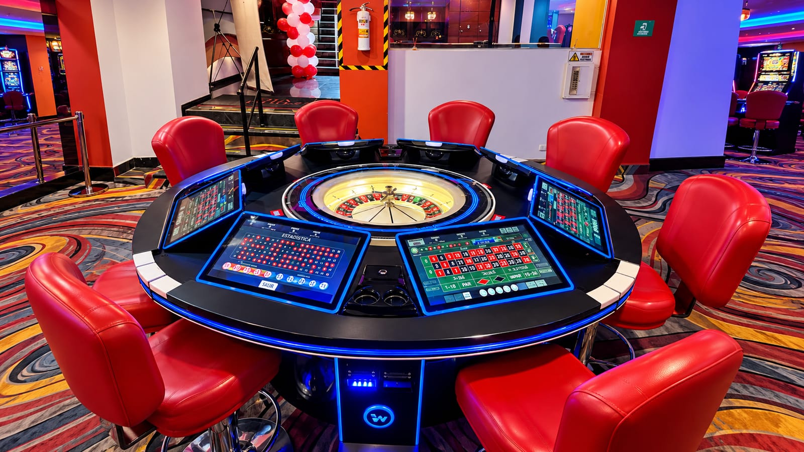 Mesa de ruleta electrónica con sus pantallas táctiles y sillas rojas alrededor en una de nuestras salas