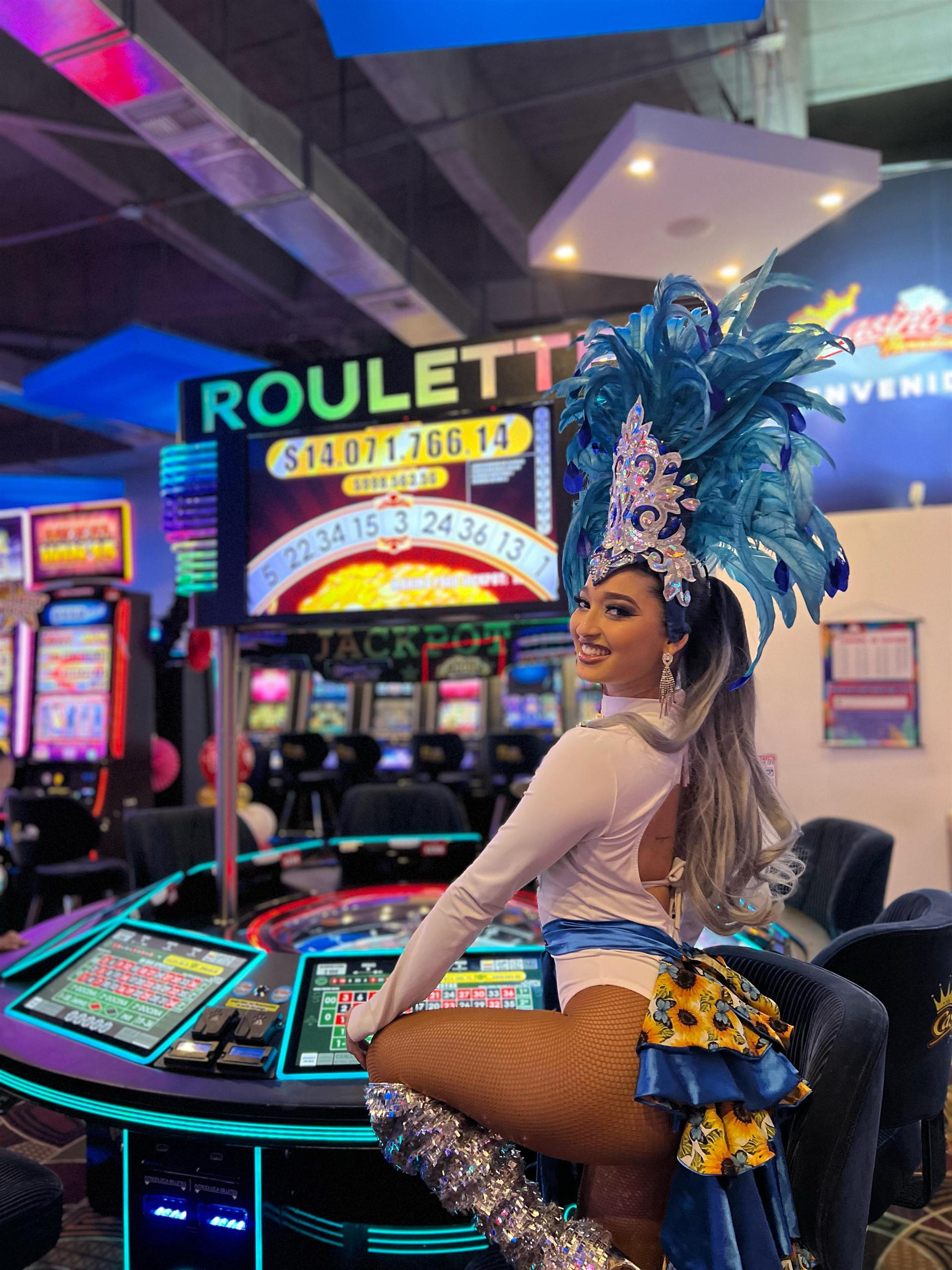 Mujer con traje de carnaval y tocado de plumas azules junto a una ruleta electrónica